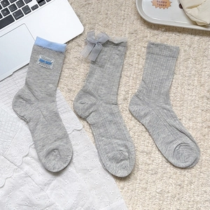 Détail de trois chaussettes grises avec bordures en dentelle, nœuds et broderies