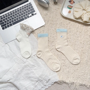 Detail of preppy style mid-calf socks with lace edges and embroidered bow on a soft rug