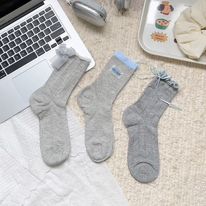 Trois modèles de chaussettes grises avec nœuds en dentelle et broderie sur un bureau