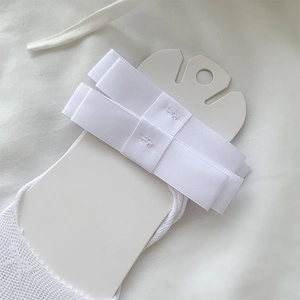 Close-up of white lace mesh sock with ribbon bow detail on white cardboard packaging