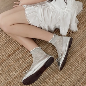 Silver ballet flats with bow and grey frilly socks on a natural woven carpet