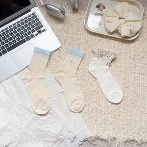 Close-up of Japanese style crew socks with bow embroidery and lace trim on a cozy rug