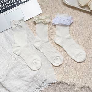 Detailed close-up of white Lolita style socks with lace bows and ruffled edges on soft carpet
