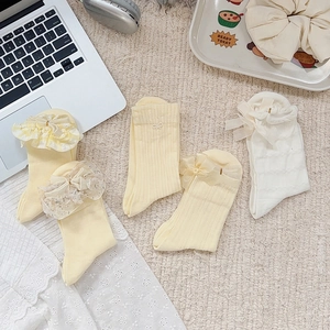 Detailed view of four pairs of cream yellow and beige lace bow socks for toddler girls
