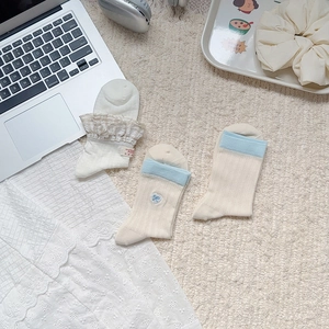 Detailed view of three pairs of cream and blue cotton socks with lace and heart embroidery