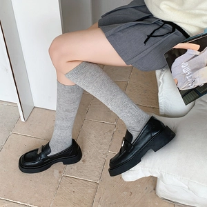 Detail of grey ribbed knee-high socks paired with black platform loafers and metal buckle