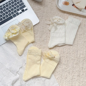 Detail of cream and yellow lace ruffle socks with bow accents on a textured rug