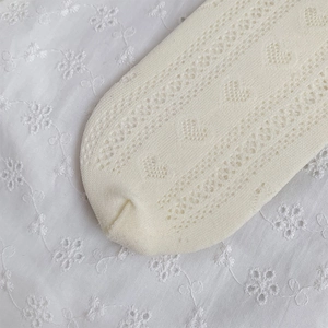 Macro detail of cream knit socks featuring heart-shaped pointelle and delicate texture