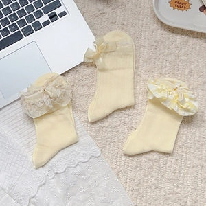 Detailed view of cream yellow ballet-style socks with lace ruffles and silk bows