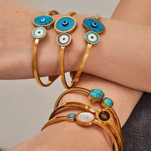 Detail of bohemian gold-plated bracelets featuring evil eye motifs and turquoise inlay