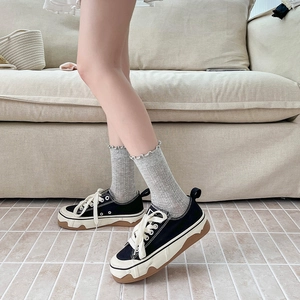 Detail of black canvas shoe with wavy platform sole and white laces on foot