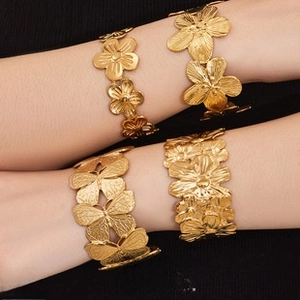Detailed close-up of 18k gold plated bracelets with butterfly and relief floral patterns