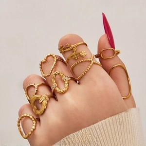 Detail of 10-piece gold floral and geometric ring set layered on hand with pink nails