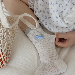 Détail de chaussette en résille avec broderie ours et décoration de nœud à carreaux bleus