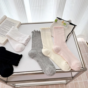 Detail of five pairs of ribbed cotton socks with wavy ruffle cuffs in neutral tones