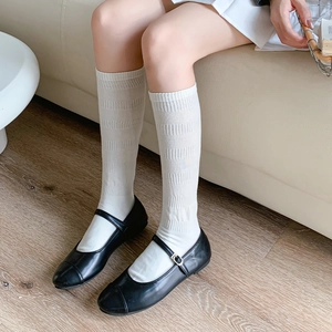 Detail of white ribbed knee-high socks paired with black Mary Jane shoes on wood floor