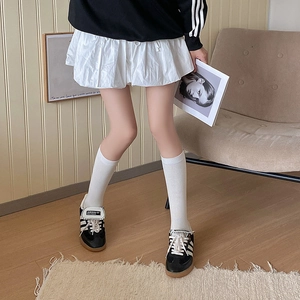Detailed view of white calf socks styled with pleated skirt and casual sneakers