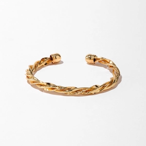 Détail d'un bracelet doré torsadé avec embouts sphériques sur fond gris clair épuré