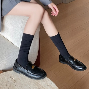 Close-up of black leather loafers with gold coin buckle paired with black crew socks