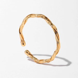 Détail d'un bracelet jonc torsadé doré avec texture croisée et finition polie
