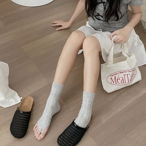 Detail of light gray flip-flop socks paired with black woven shoes on wood floor