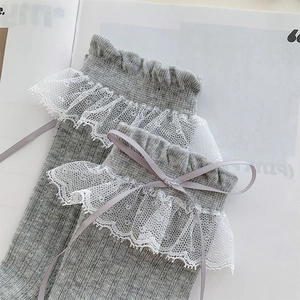 Détail de la dentelle blanche et du nœud en soie violette sur des chaussettes en tricot