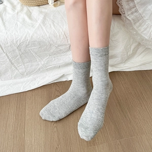 Détail de chaussettes mi-hautes côtelées gris clair sur un sol en bois naturel