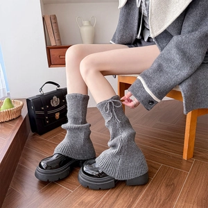 Close-up of grey knitted leg warmers with vertical ribs and delicate bow tie detail