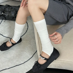 Close-up of white vertical ribbed knit leg warmers paired with black ballet flats