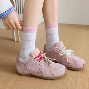 Pink suede sneakers with striped crew socks on wooden floor lifestyle view