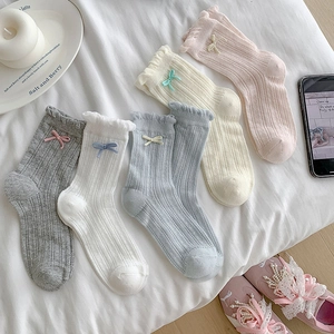 Flat lay of five pairs of pastel mesh socks with ruffles and bows on white sheets