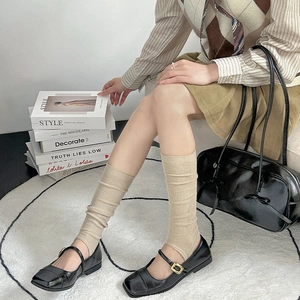 Close-up of beige ribbed knit leg warmers paired with black Mary Jane shoes