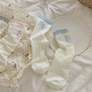 Détail de broderie d'ours et bouton cœur sur chaussettes en maille ajourée respirante