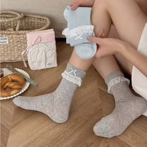 Dettaglio di calze in maglia morbida con bordo in pizzo bianco e decoro a fiocco
