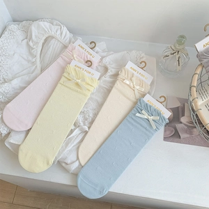 Flat lay of four colorful knit mid-calf socks with ribbon bows and wavy lace edges