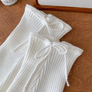 Macro detail of white ribbed knit leg warmers with delicate bow tie strings on wood