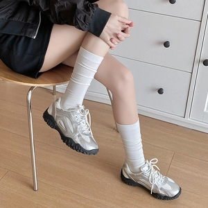 Close-up of silver metallic chunky sneakers with white laces on a model indoors