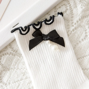 Close-up of Lolita socks featuring white ribbed knit, black bow, and pearl pendants