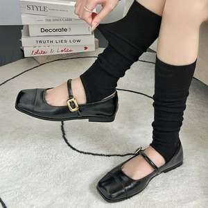 Detail of ribbed knit leg warmers paired with black Mary Jane shoes on a plush rug