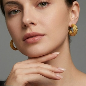 Close-up of chunky gold hoop earrings with woven texture on a model's ear