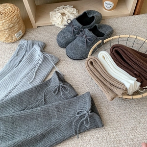 Detail of knitted leg warmers with ribbon bows paired with grey felt mule shoes