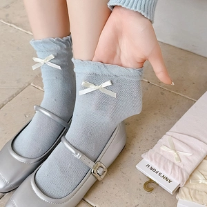 Detail of light blue mesh socks with white bow and ruffle cuff worn with silver shoes