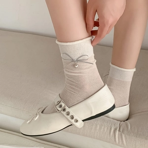 Detail of white knit sock featuring a silver bow and heart pendant with Mary Jane shoe