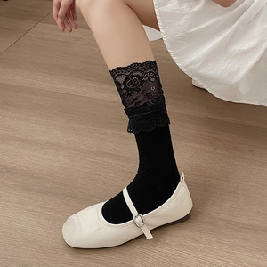 Detailed view of black lace socks paired with white leather Mary Jane shoes on wood floor
