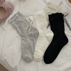 Dettaglio delle calze a rete con fiocchi di pizzo nei colori grigio, bianco e nero chic