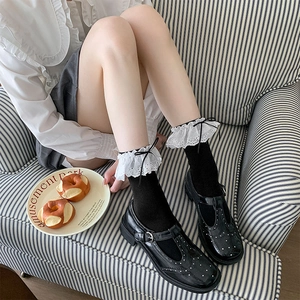 Detail of white lace ruffle socks with bow decoration worn with black Mary Jane shoes