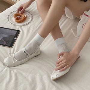 White ballet flats with bow and elastic straps paired with heart lace socks on white bedding