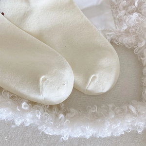 Close-up of creamy white knitted socks with soft wool background showing smooth toe seams