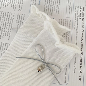 Detail of white ruffle socks featuring silver ribbon bows and metallic heart pendants