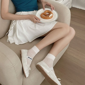 Close-up of white satin ballet flats with bow detail and sheer polka dot crew socks